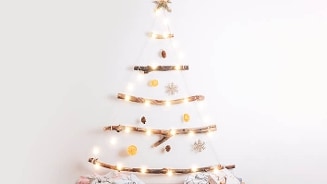 Minimalistische kerstboom gemaakt van takken en verlichte lampjes versierd met dennenappels en decoraties aan de muur.