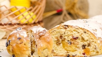 Ambachtelijk gesneden stol met rozijnen, noten en poedersuiker, op de voorgrond met op de achtergrond een mand met eieren.