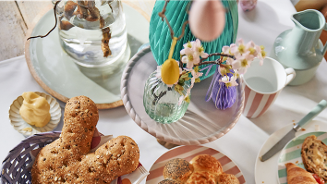 Paastafel met broodjes, decoratie en een vaas met bloemen.