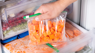 Hand die diepvrieszak met stukjes wortel uit diepvrieslade pakt