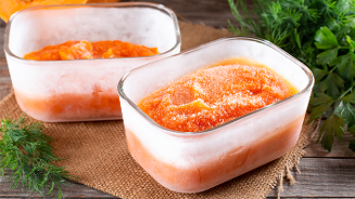 Diepvriesbakjes met ingevroren pompoenpuree op houten ondergrond, omringd door verse kruiden