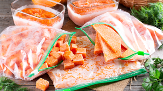 Diepvrieszakken gevuld met bevroren stukken en blokjes pompoen op een houten ondergrond, omringd door verse kruiden