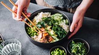 Poké bowl met zalm, rijst, komkommer, edamame en koriander, geserveerd in een kom.