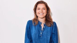 Vrouw met lang bruin haar in een spijkerblouse tegen een lichte achtergrond