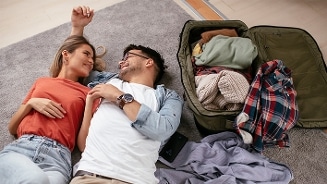 Stel ligt samen op een tapijt naast een open koffer met kleding