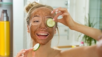 Persoon brengt een plakje komkommer aan op de huid in een badkamer