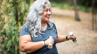Vrouw met grijs haar oefent buiten met kleine halters