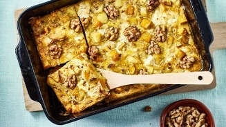 Ovenschotel met aardappel, kaas en walnoten, geserveerd in een bakvorm met een houten lepel