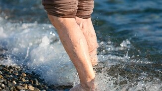 Blote benen van een persoon lopen door ondiep water langs een kiezelstrand