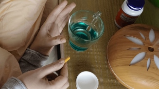 Glas met blauwe vloeistof, hand met vitaminepil en potje op nachtkastje