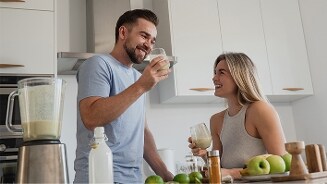 Man en vrouw in een moderne keuken drinken groene smoothie, met blender en verse appels op het aanrecht