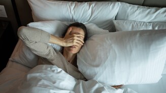 Persoon ligt in bed onder witte dekens met meerdere kussens