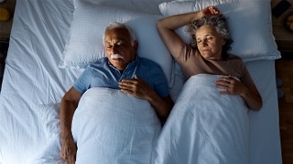 Oud stel ligt samen in bed onder witte dekens