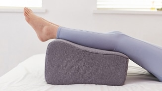 Persoon met opgetilde benen die rusten op een ergonomisch kussen op bed
