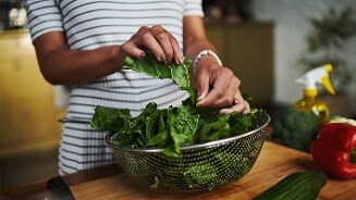 Persoon wast verse groene bladgroenten in een vergiet op een keukentafel met paprika en komkommer