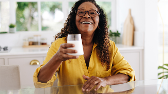 Persoon in een gele blouse houdt een glas melk vast in een lichte keuken.