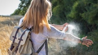 Vrouw met rugzak die insectenspray op haar arm spuit in de natuur