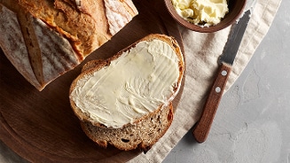Volkorenbrood gesmeerd met boter naast een mes en een schaaltje boter.