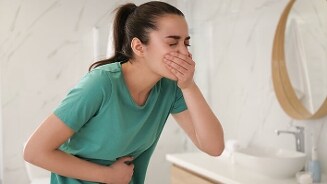 Persoon met maagklachten leunend over een wastafel in de badkamer.