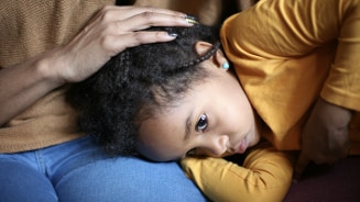 Persoon die knuffelt met een kind in gele kleding, hoofd rustend op schoot.