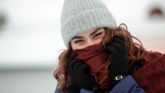 Persoon met een grijze gebreide muts, zwarte handschoenen en rode sjaal in een winterse omgeving