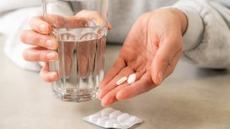 Persoon houdt witte pillen in de hand met een glas water.