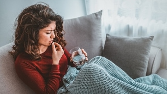 Vrouw onder een deken met een glas water zittend op een bank.