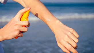 Persoon brengt zonnebrandcrème aan op arm bij het strand