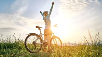 Persoon op een fiets met armen uitgestrekt, genietend van de zonsondergang in een grasveld.