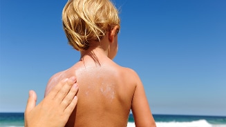 Kind krijgt zonnebrandcrème op de rug aangebracht op het strand