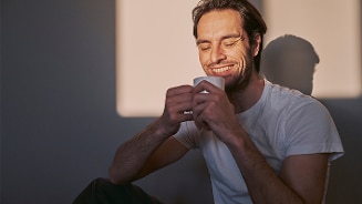 Man in wit shirt zittend tegen een muur met schaduw in achtergrond.