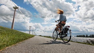 Vrouw fietst langs windmolens op een zonnige dag.
