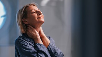 Persoon in blauwe blouse houdt handen tegen de nek