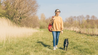 Vrouw wandelt met een zwarte hond op een grasveld met bomen op de achtergrond.