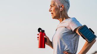 Persoon met oordopjes en smartphone armband, drinkend uit een rode waterfles.