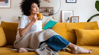 Persoon ontspant op een gele bank met een boek en een kopje koffie.