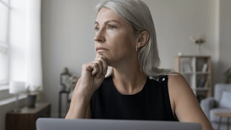 Vrouw met grijs haar in een woonkamer, zittend achter een laptop.