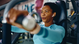 Persoon aan het trainen op een fitnessapparaat met oordopjes in.