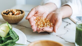 Handen met visoliecapsules naast groenten en noten.