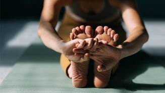 Vrouwelijke yogabeoefenaar in een zittende vooroverbuiging op een yogamat.
