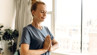 Vrouw die yoga beoefent bij het raam van haar woonkamer.