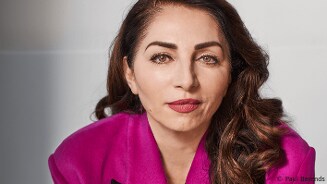 Vrouw in felroze kleding met halflang, krullend bruin haar.