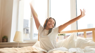 Persoon die zich uitrekt in bed bij het raam in een zonnige slaapkamer.