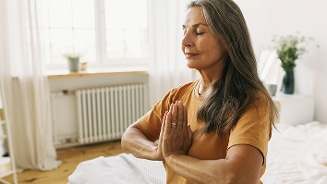 Persoon in meditatiehouding in een lichte kamer met planten in de achtergrond.