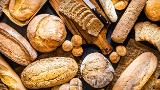 Verschillende soorten brood en broodjes, waaronder volkorenbrood, stokbrood en kaiserbroodjes.