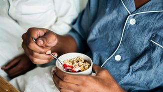 Persoon in pyjama eet ontbijt met yoghurt, granola en aardbeien op bed
