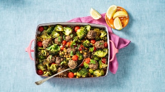 Ovenschotel met gehaktballen, broccoli, kikkererwten en cherrytomaten, geserveerd met citroenpartjes.