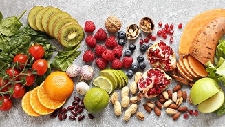 Assortiment van vers fruit, noten en groenten op een grijze ondergrond.