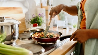 Persoon kookt groenten in een pan op het fornuis in de keuken.