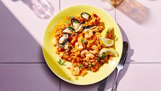 Een bord met paella, gegarneerd met mosselen, garnalen en schijfjes citroen.